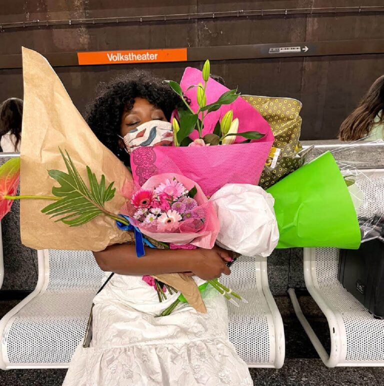 Christl Clear hält mehrere Blumensträuße, die sie bei ihrer Lesung im Volksgarten Pavillon bekommen hat während sie bei der Station Volkstheater auf die U-Bahn wartet