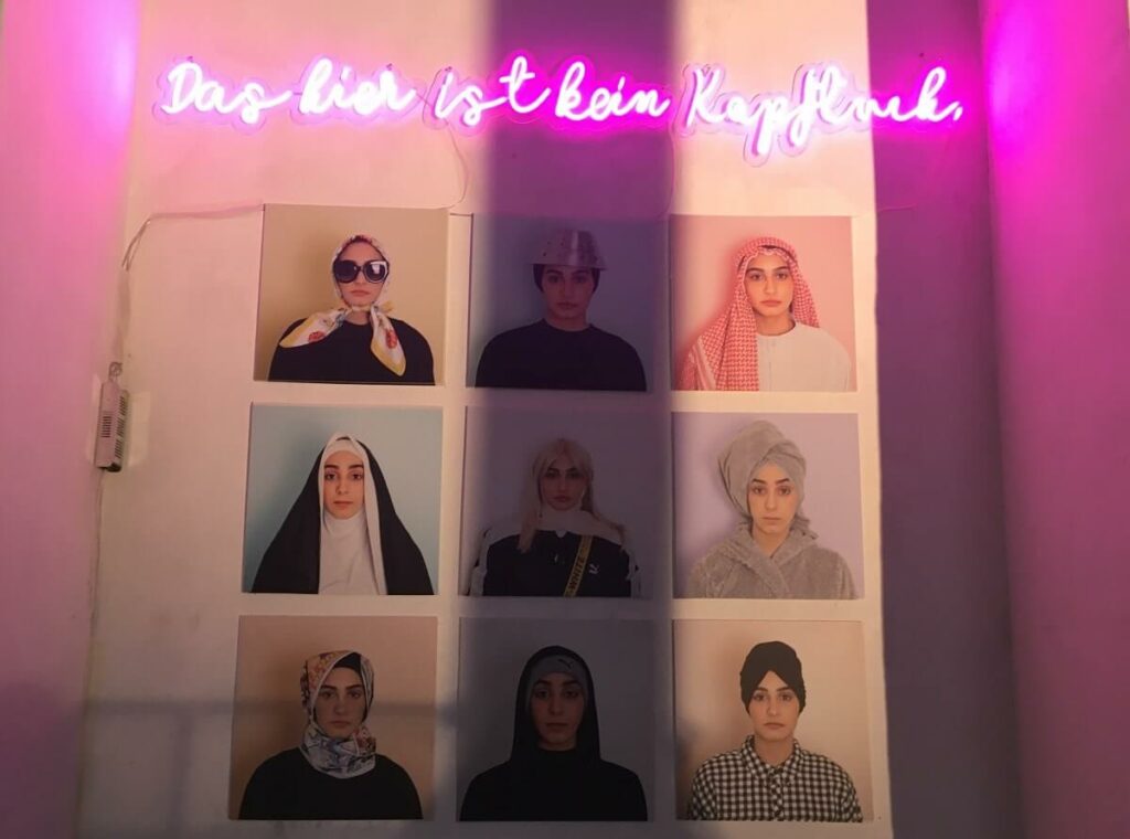 Ausstellungsstück der Muslim Contemporary: Neun Fotografien der selben Frau mit verschiedenen Kopfbedeckungen. Darüber ein pinker Neon-Schriftzug „Das hier ist kein Kopftuch“